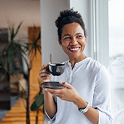 Woman smiling while drinking cup of coffee at home